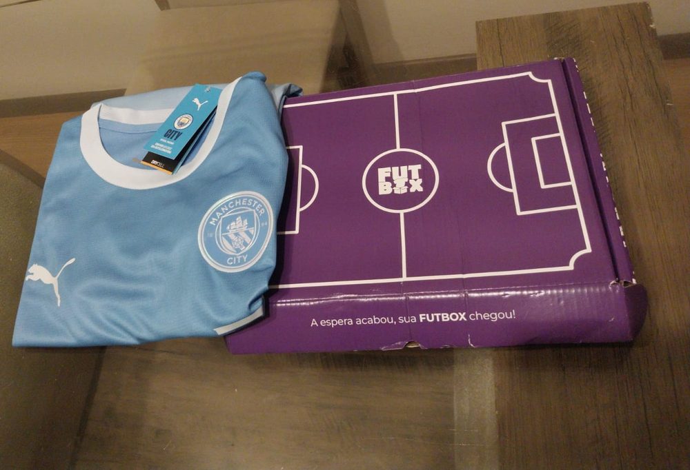 Caixa roxa da Futbox ao lado da camisa nova do Manchester City, ainda com a etiqueta